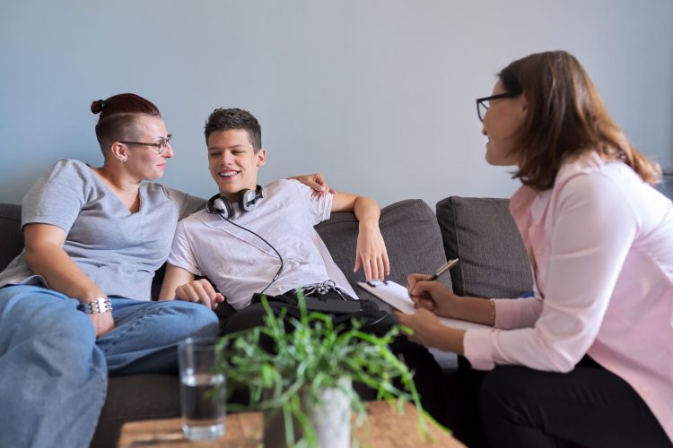 Mother with her teenage son at meeting with social worker, psychologist, discussing, mental health family, sitting on sofa in psychotherapist office